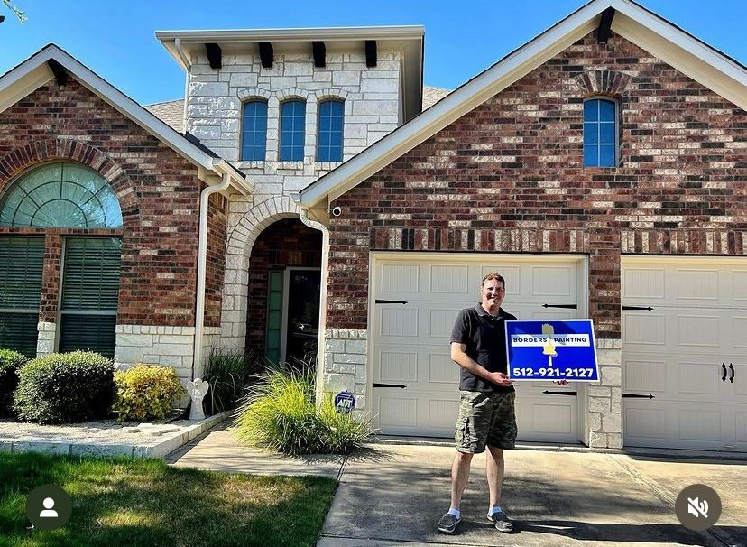 A man is standing in front of a brick house holding a sign.