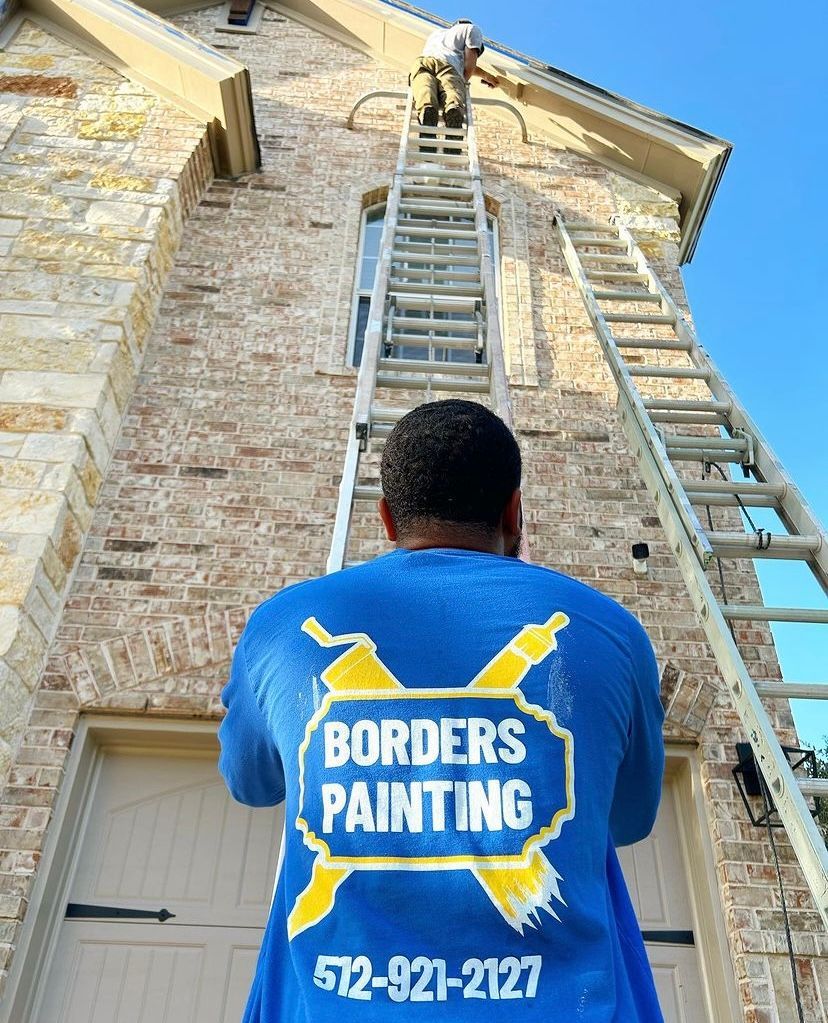A man wearing a blue shirt that says borders painting is standing on a ladder.