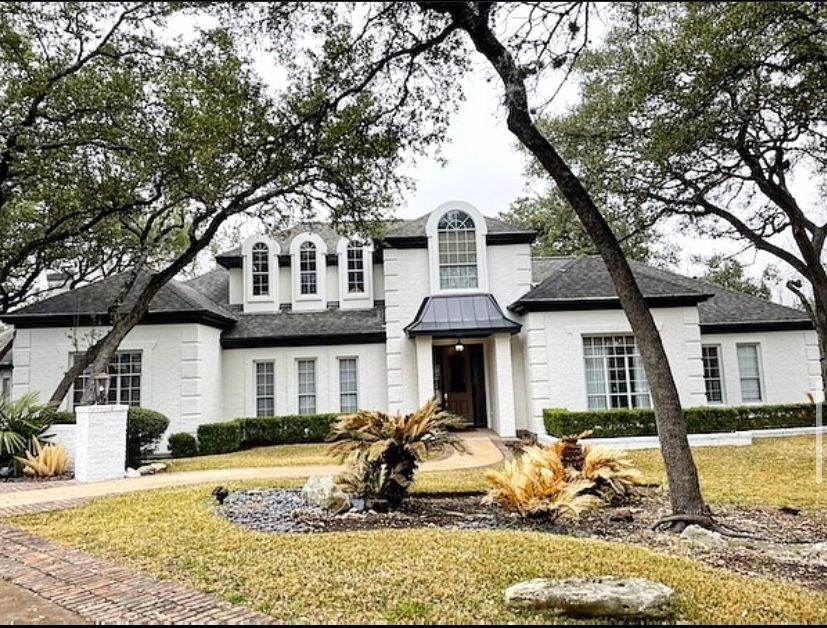 A large white house with a black roof is surrounded by trees