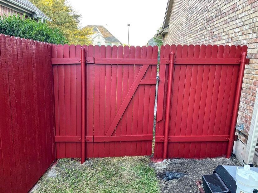 A red wooden fence with a gate in the backyard of a house.