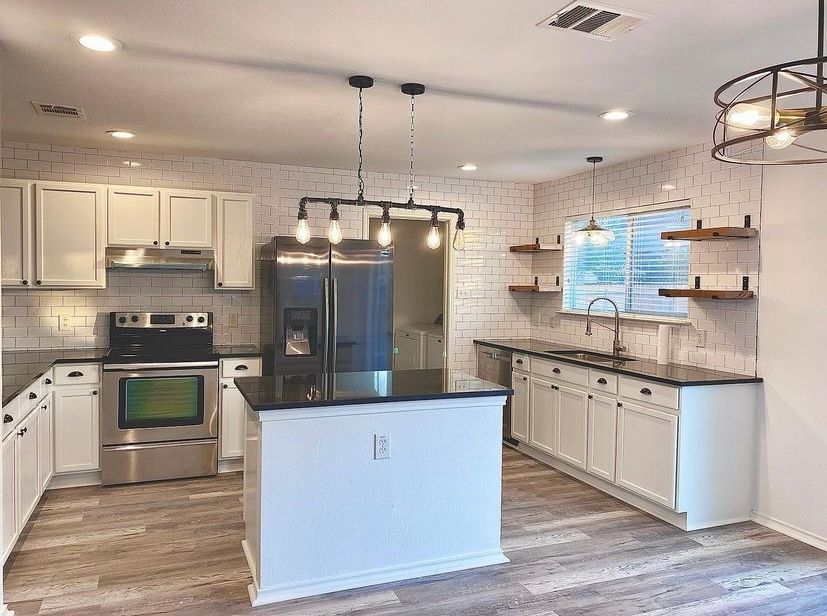A kitchen with white cabinets , stainless steel appliances , and a large island.