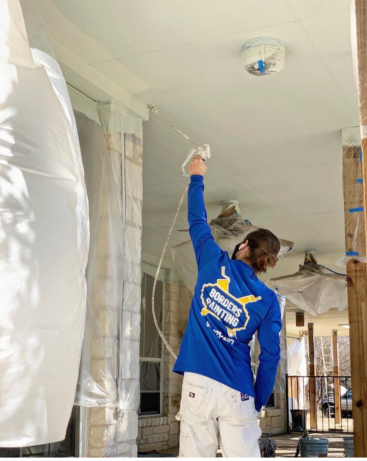 A man in a blue shirt is spray painting the ceiling of a house.