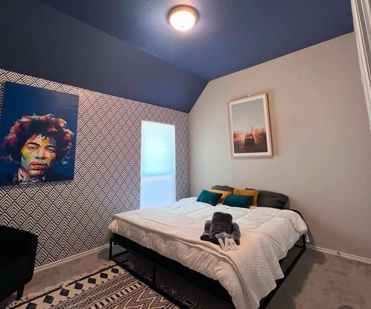 A bedroom with a bed and a painting of jimi hendrix on the wall