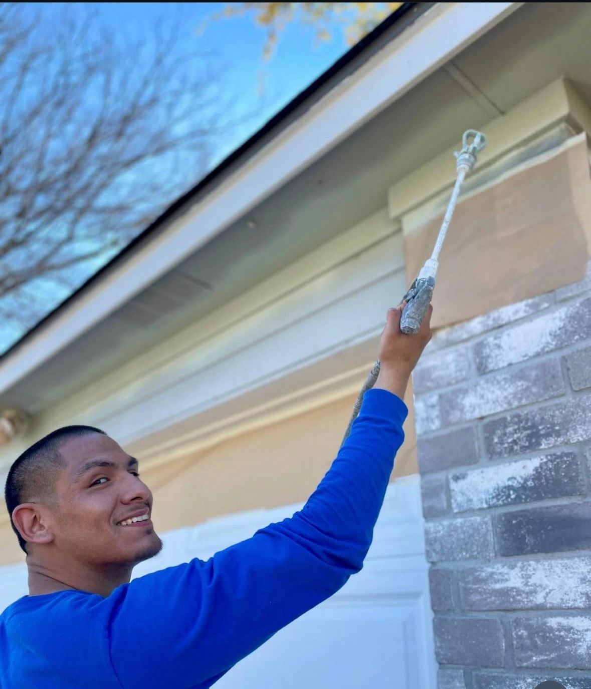 A man in a blue sweater is spraying paint on a wall