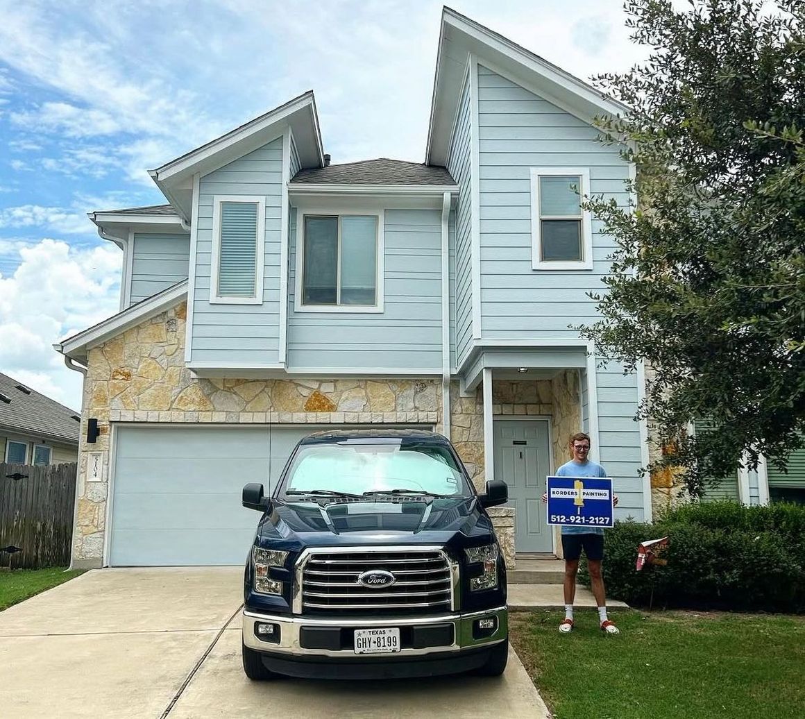 A man is standing in front of a house holding a sign.