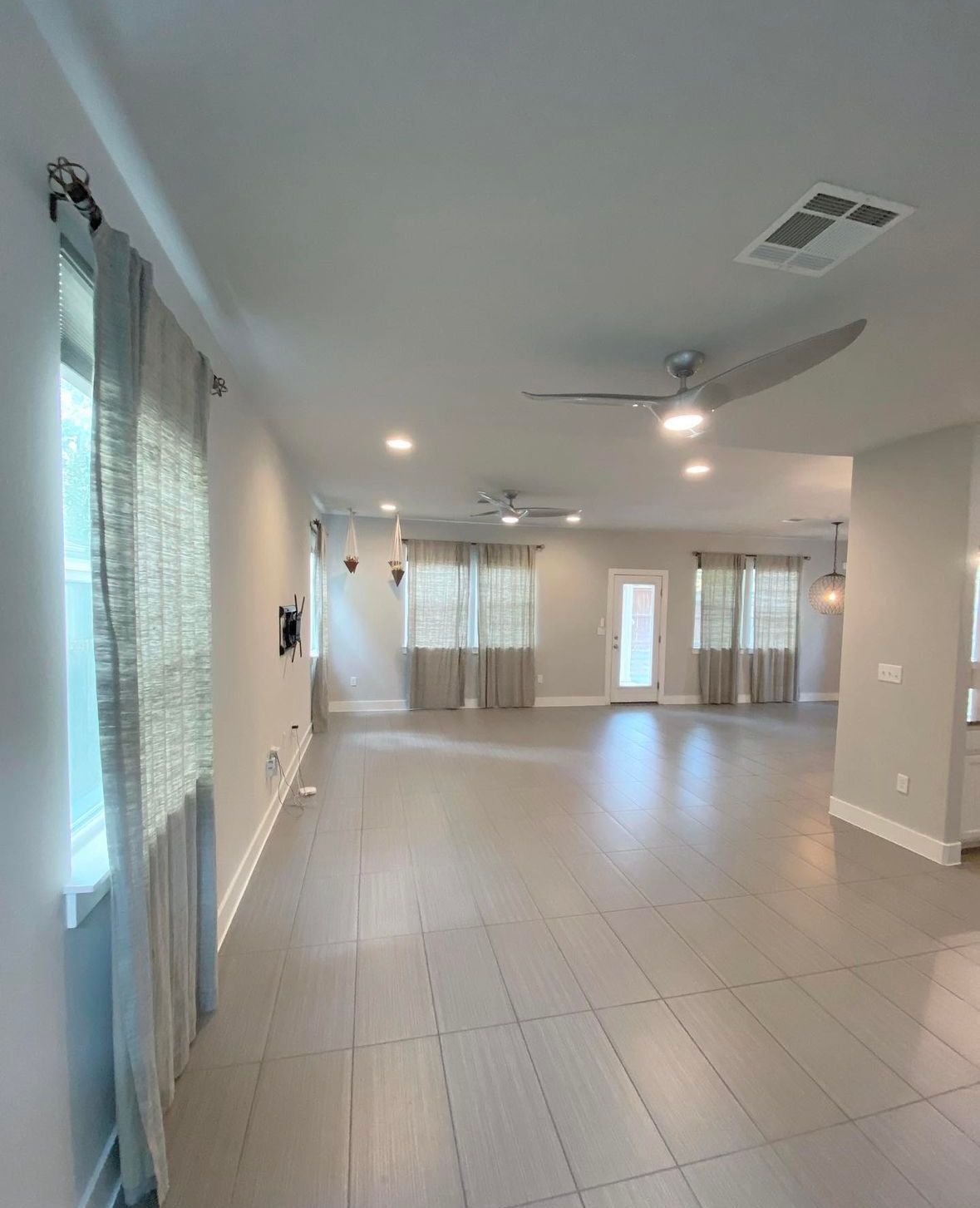 A large empty room with a ceiling fan and curtains.