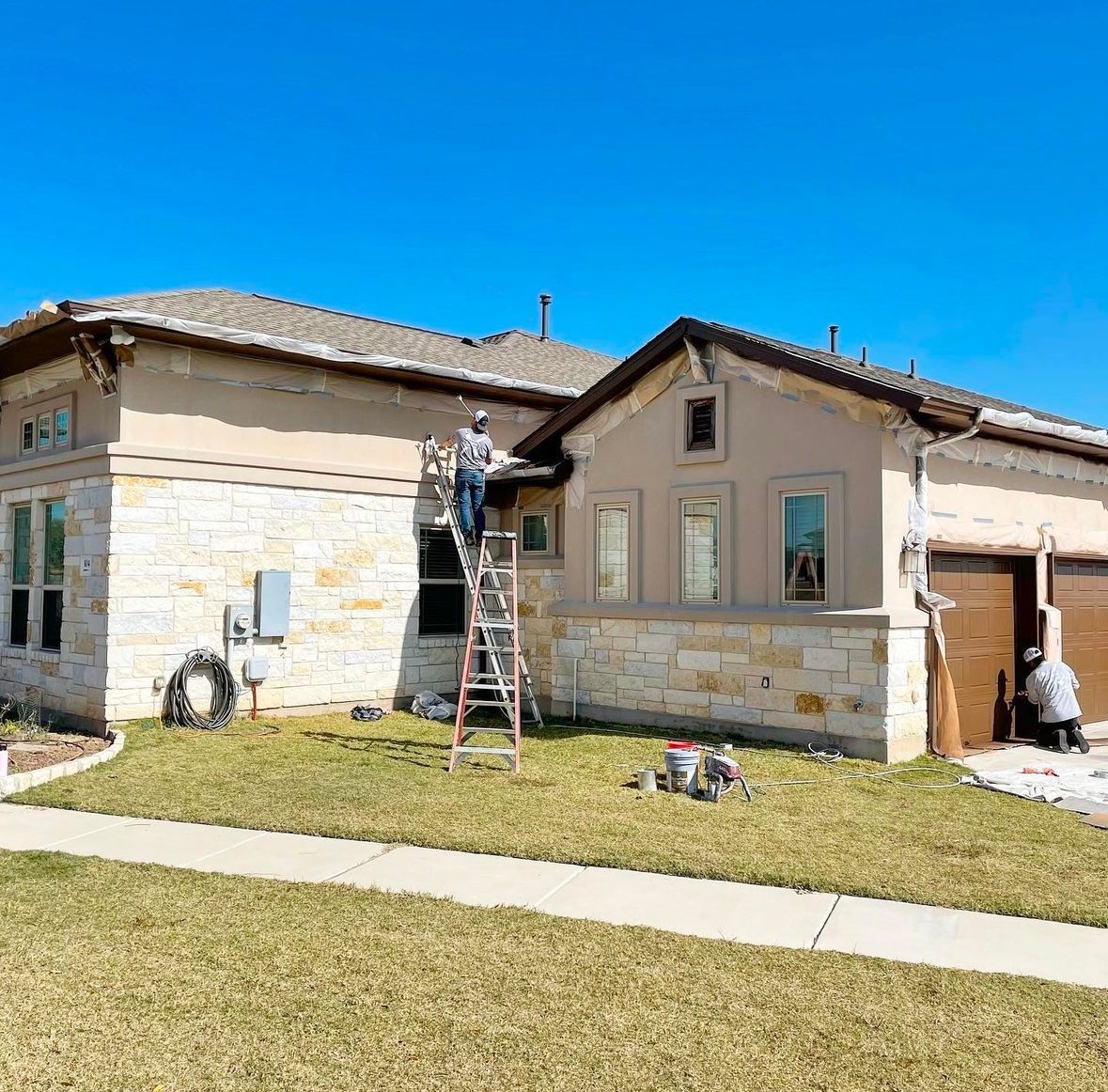 A man is standing on a ladder painting the side of a house.