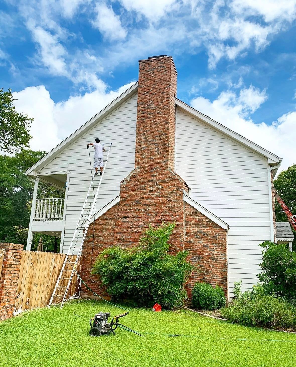 A man is painting the side of a house with a ladder.