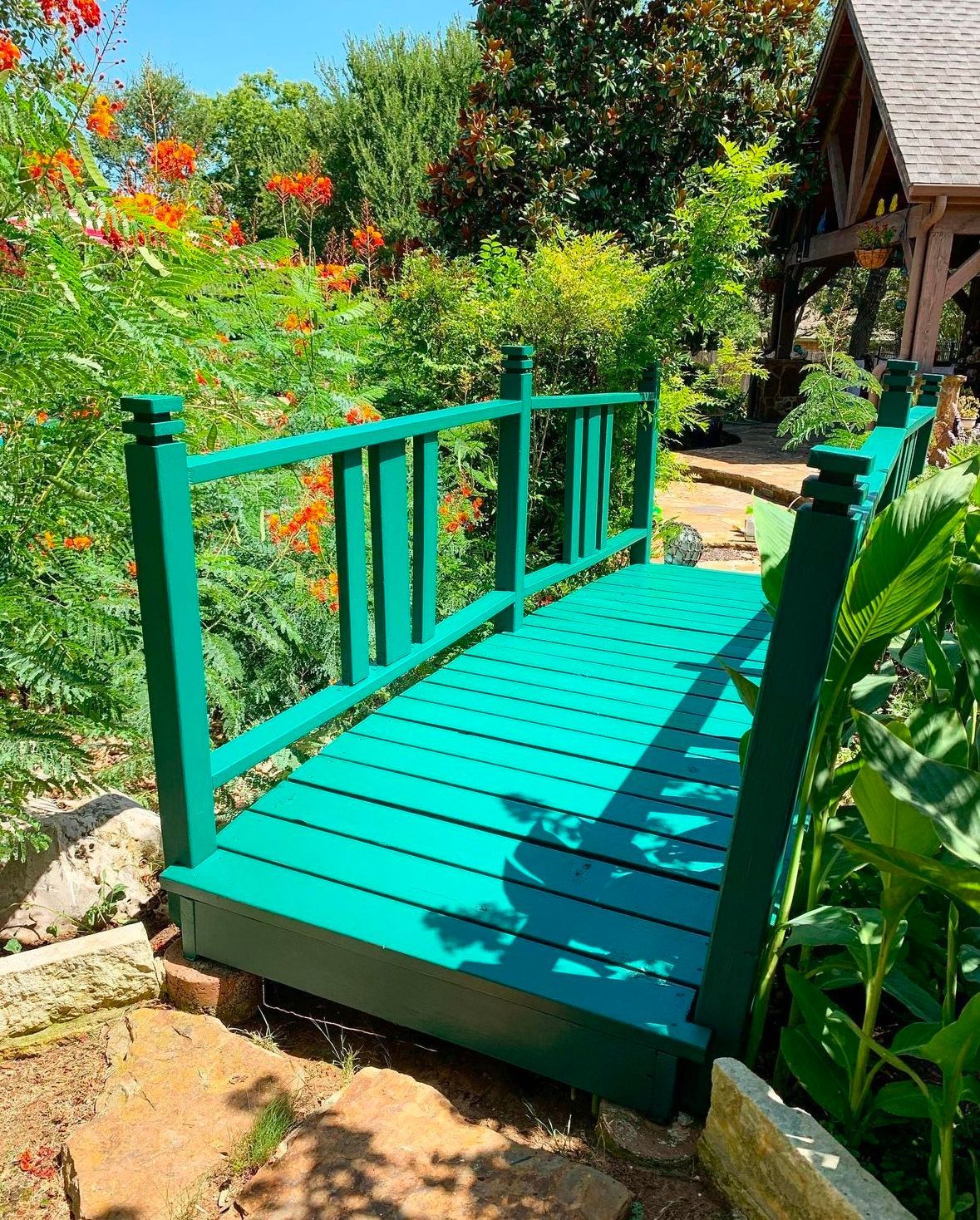 A green wooden bridge is in the middle of a garden.
