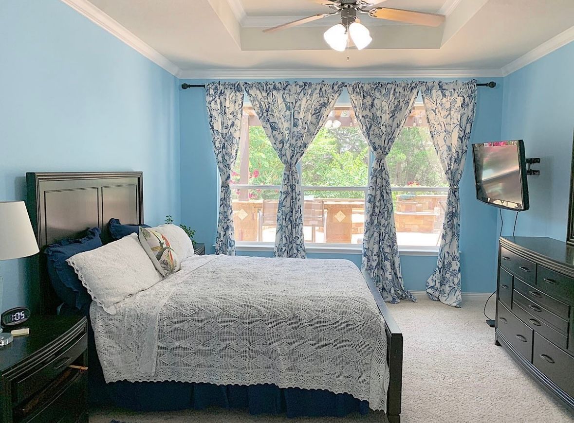 A bedroom with a bed , dresser , television and ceiling fan.