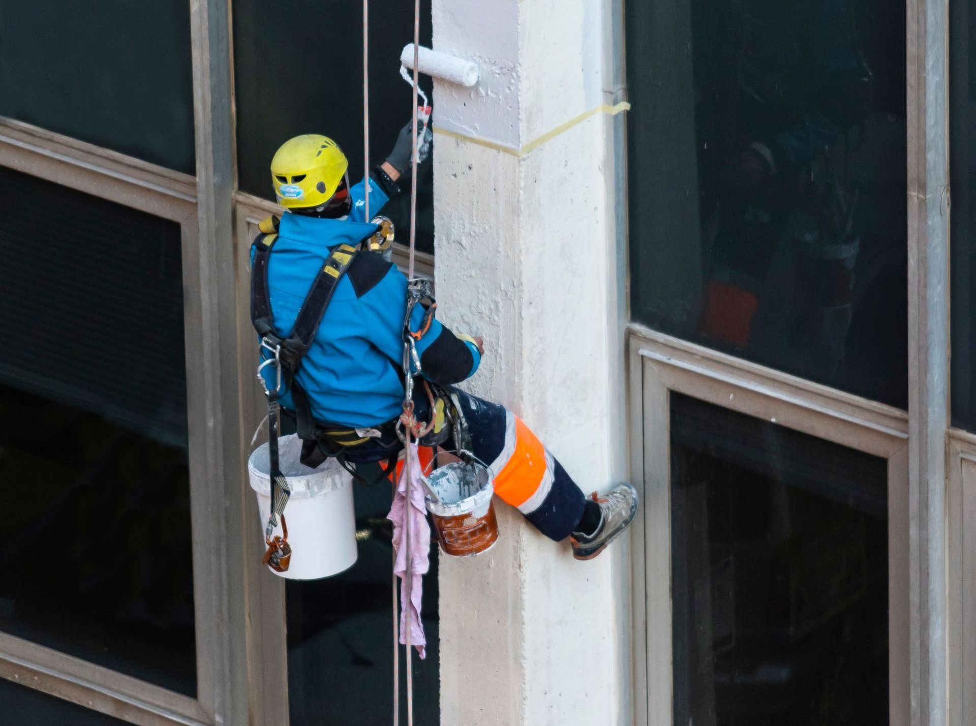 A man is climbing up a building with a bucket of paint.