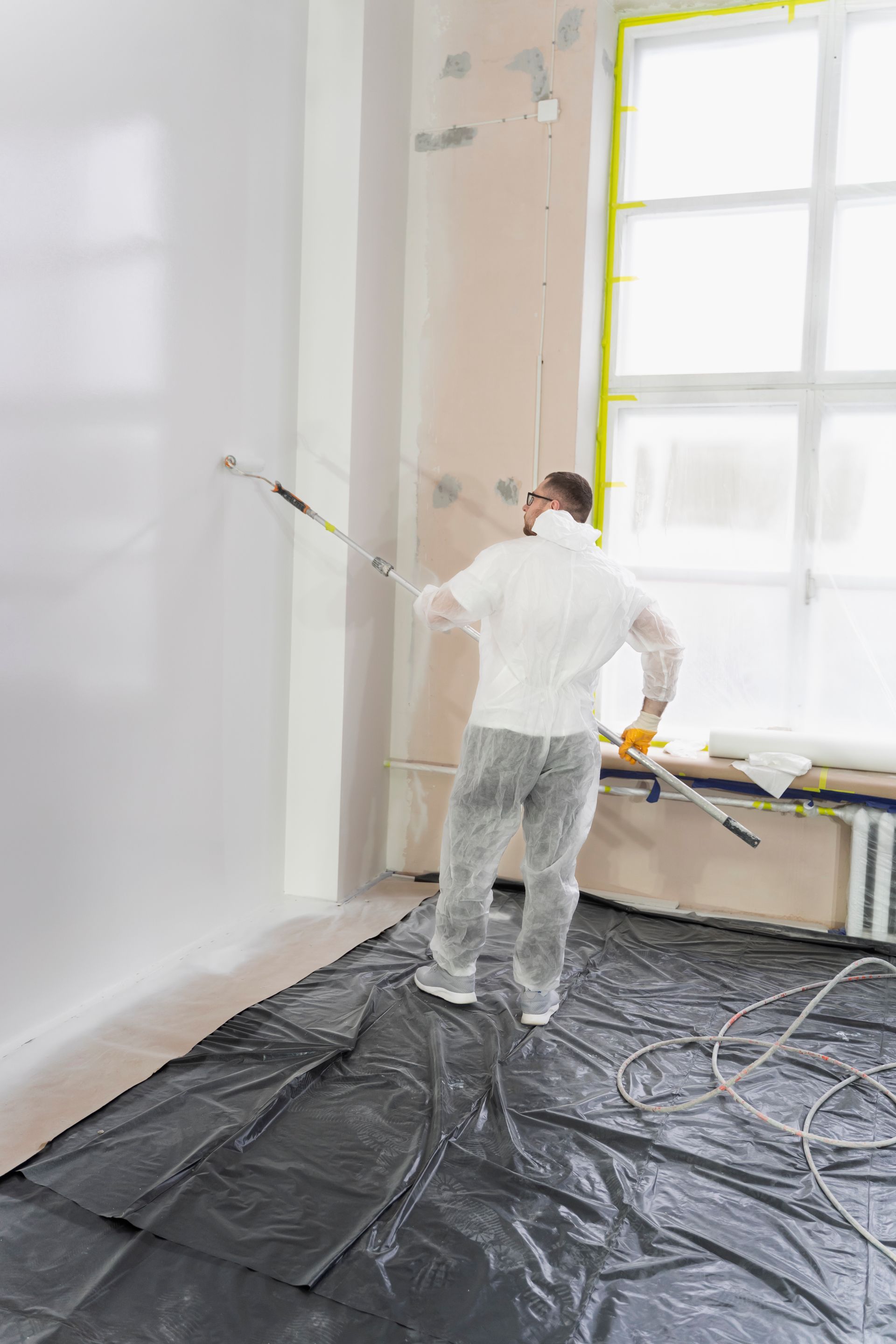A man is painting a wall with a roller in a room.