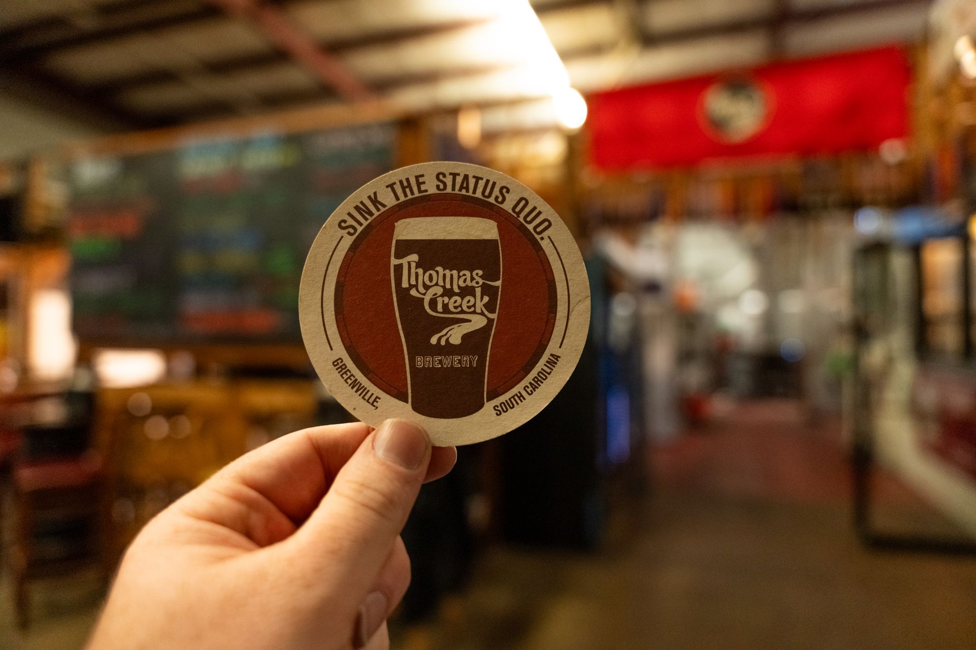 a person is holding a thomas creek beer coaster in their hand .
