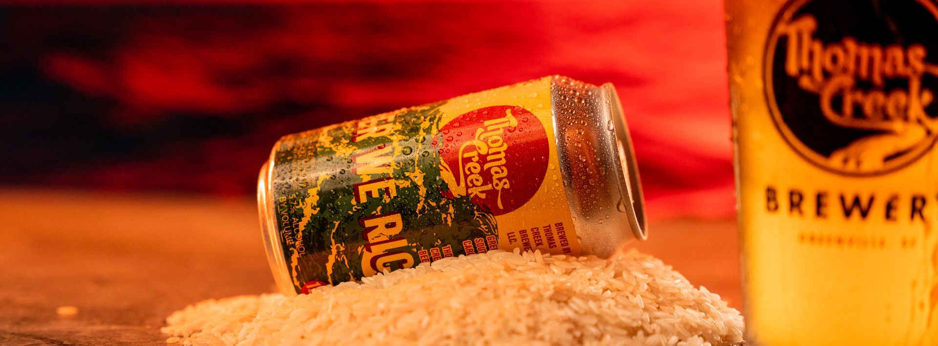 a can of beer is sitting on top of a pile of rice next to a glass of beer .