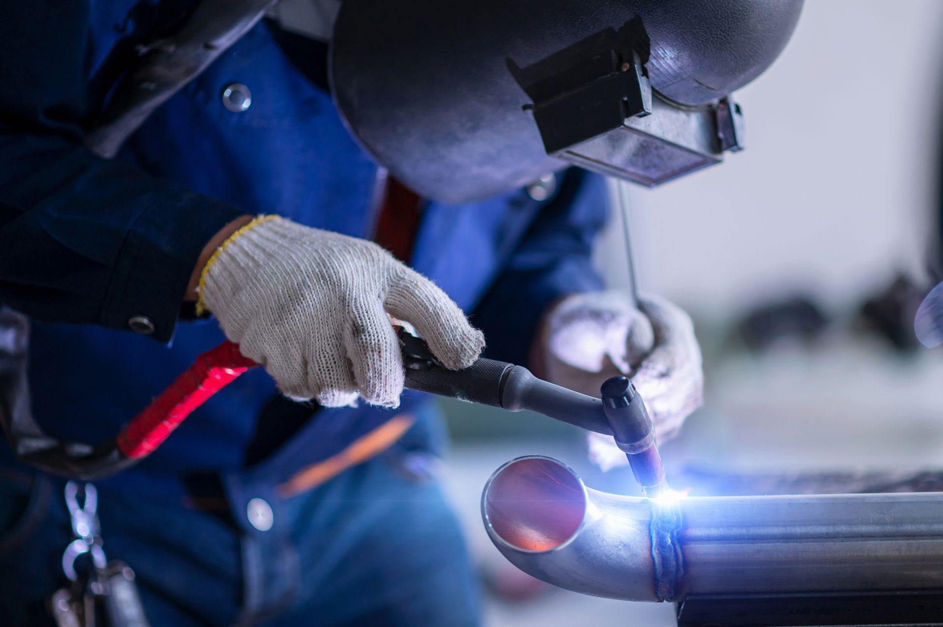 Worker welding a metal pipe with bright blue sparks during a fabrication process.