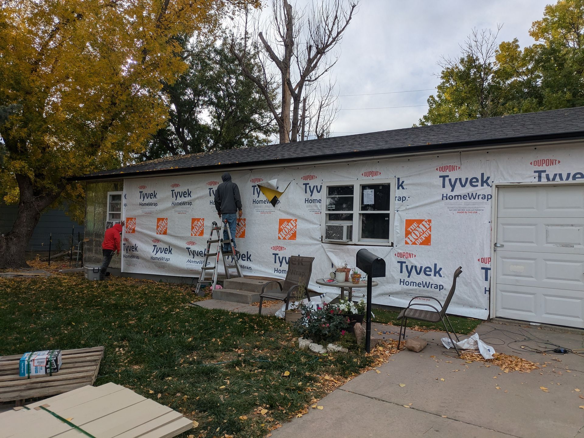 A man is standing on a ladder in front of a house that is being remodeled.