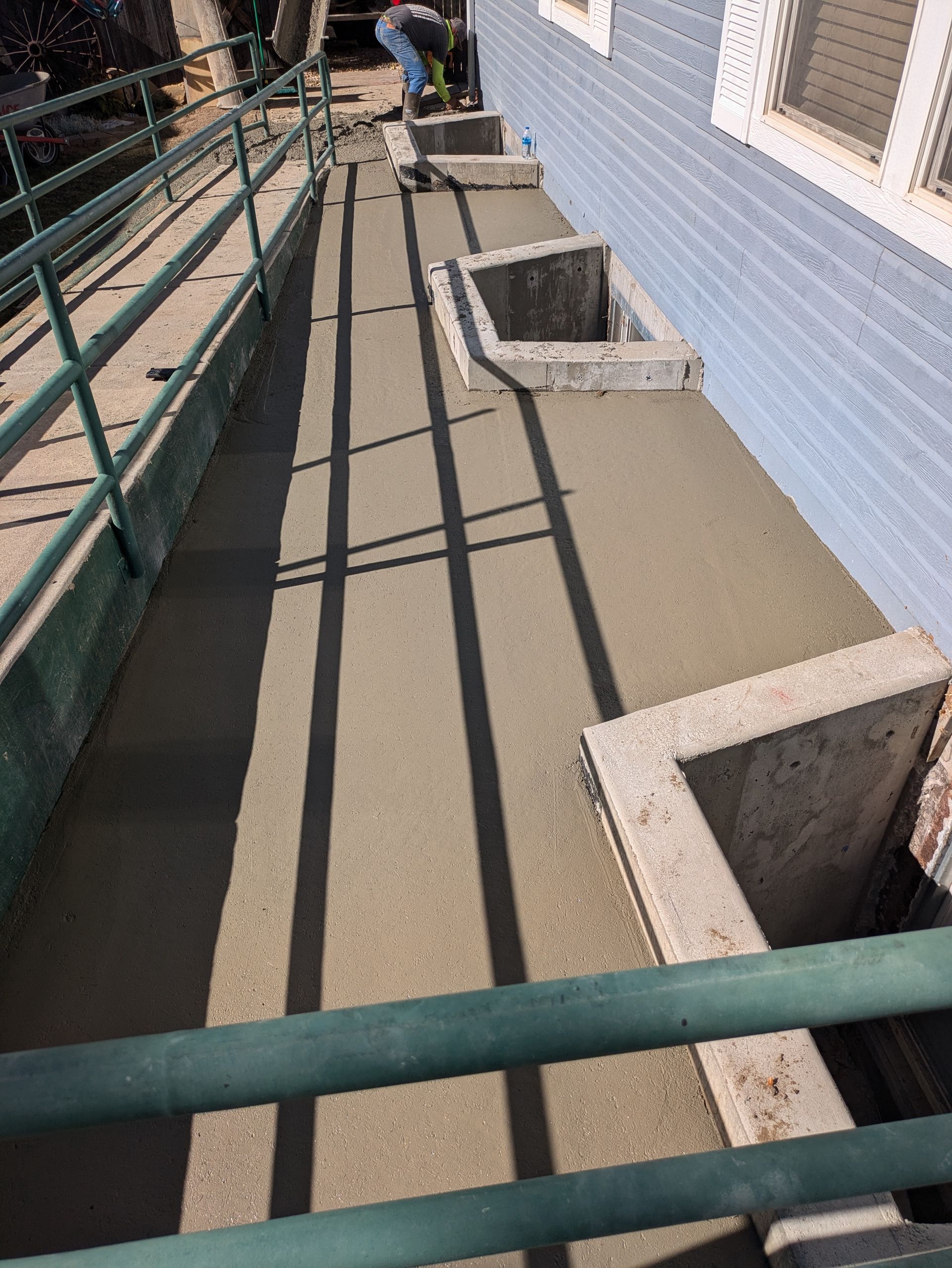 A man is working on a concrete walkway next to a building.