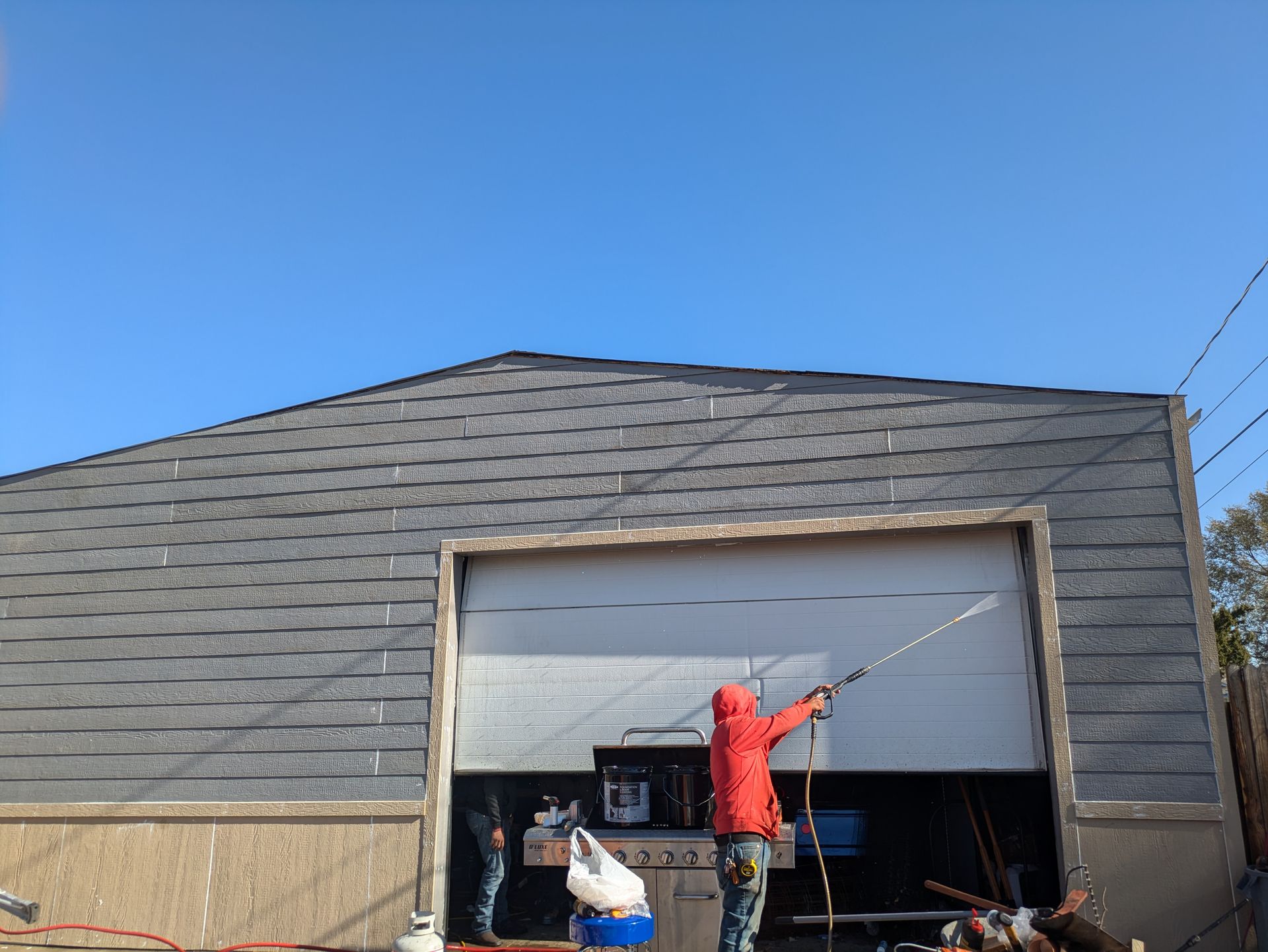A man is painting a garage door with a sprayer.