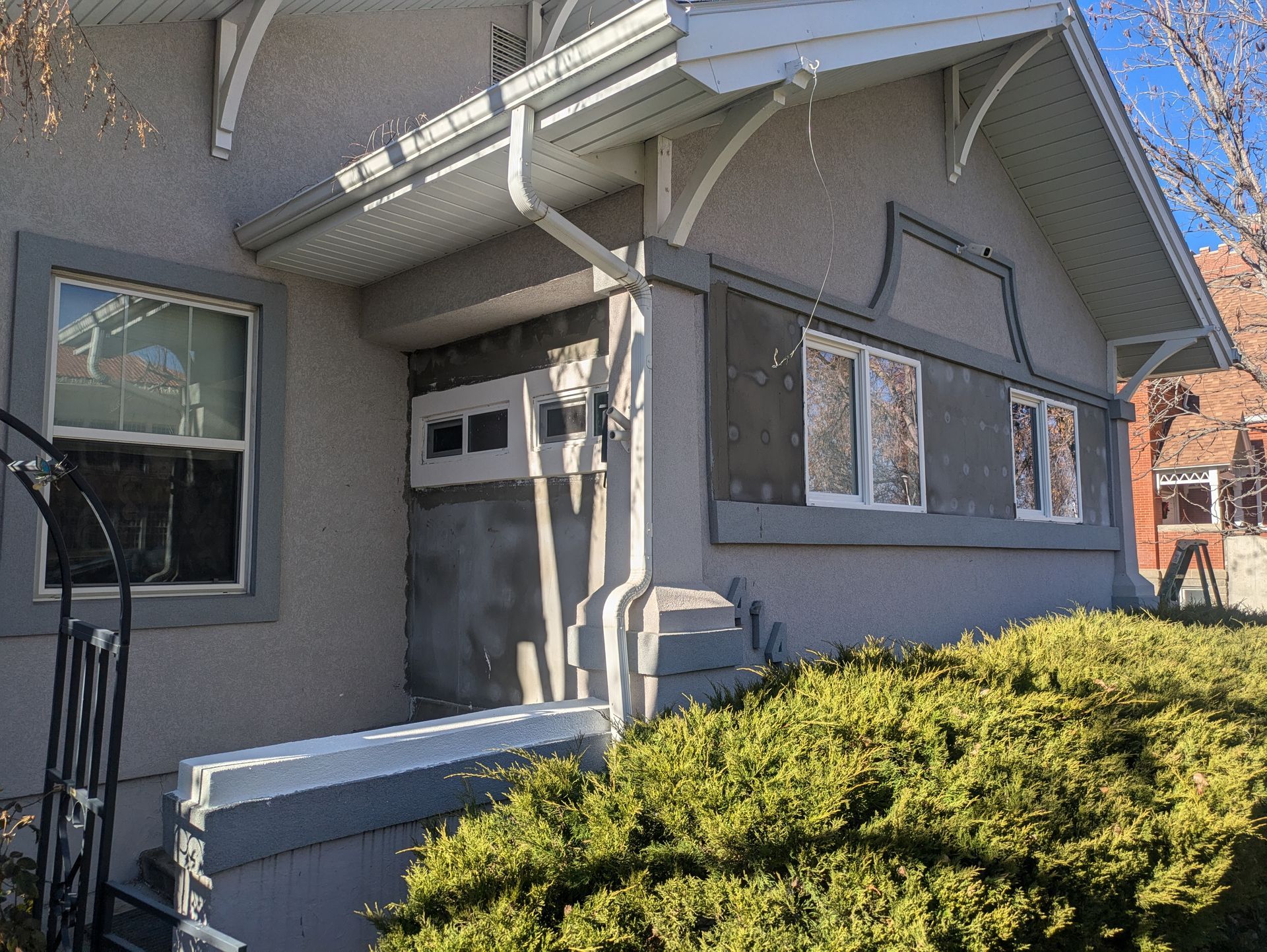 A house with a porch and a staircase is surrounded by bushes and trees.