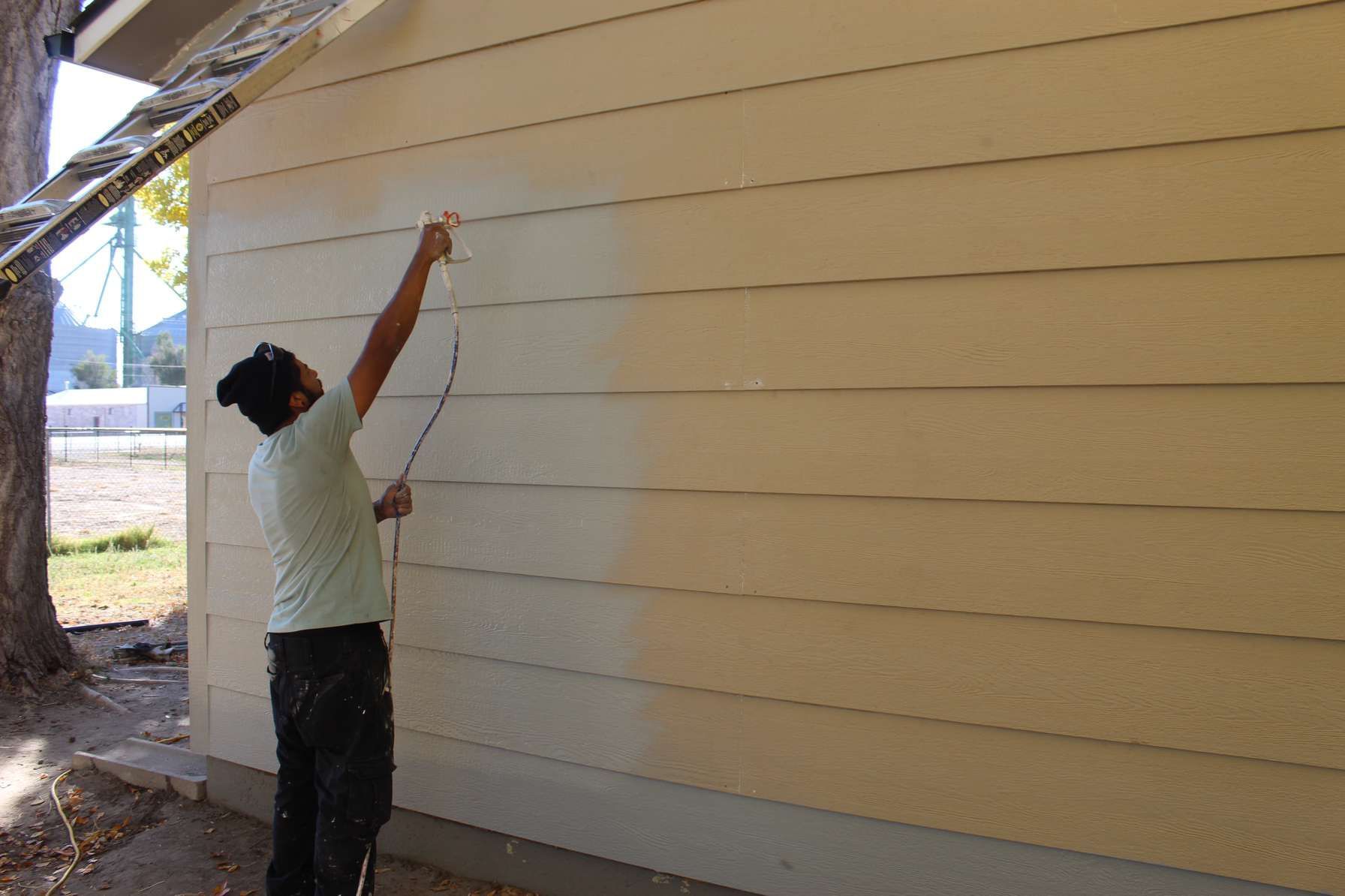 A man is painting the side of a house with a sprayer.