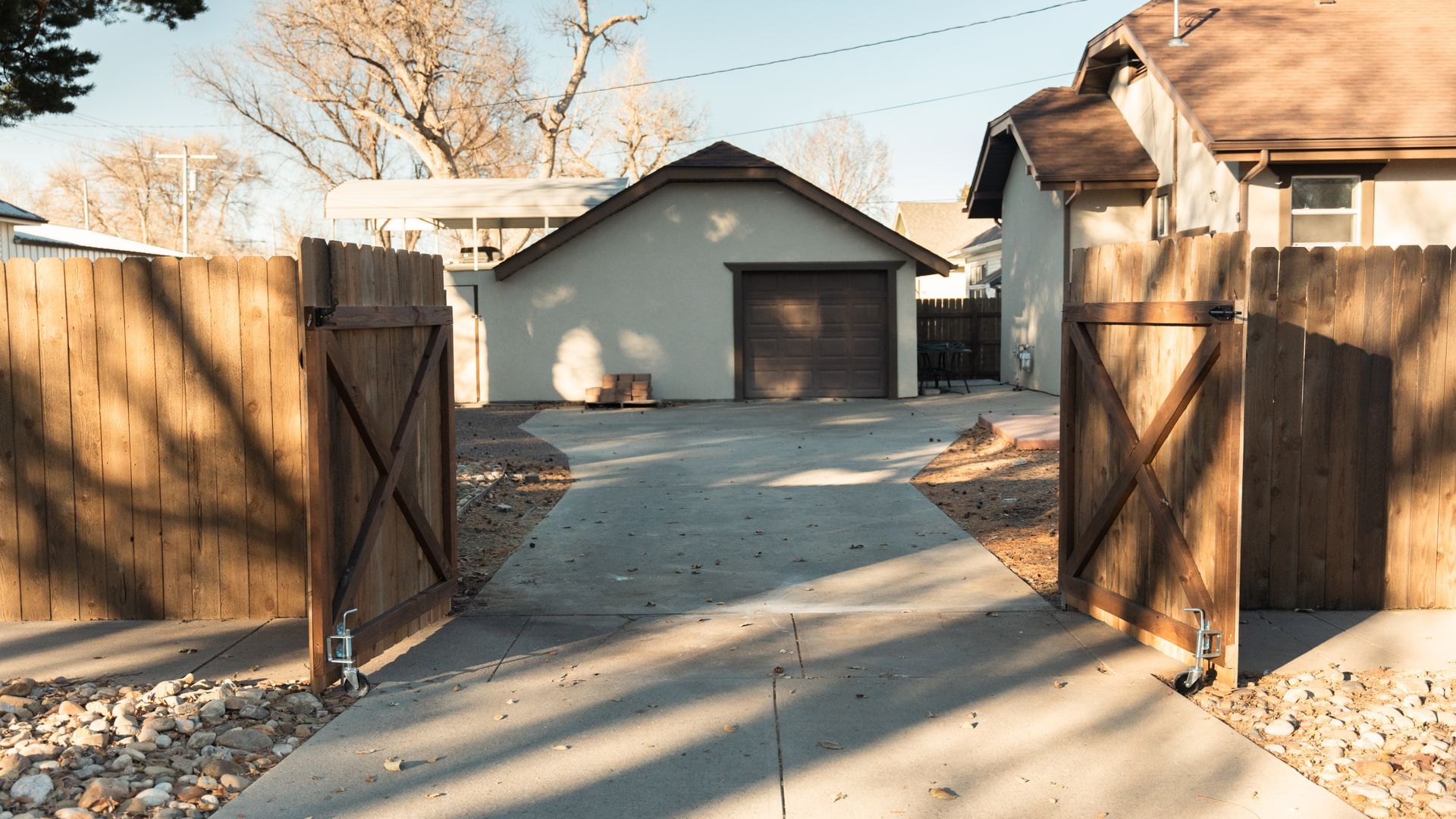A wooden fence surrounds a driveway leading to a garage.