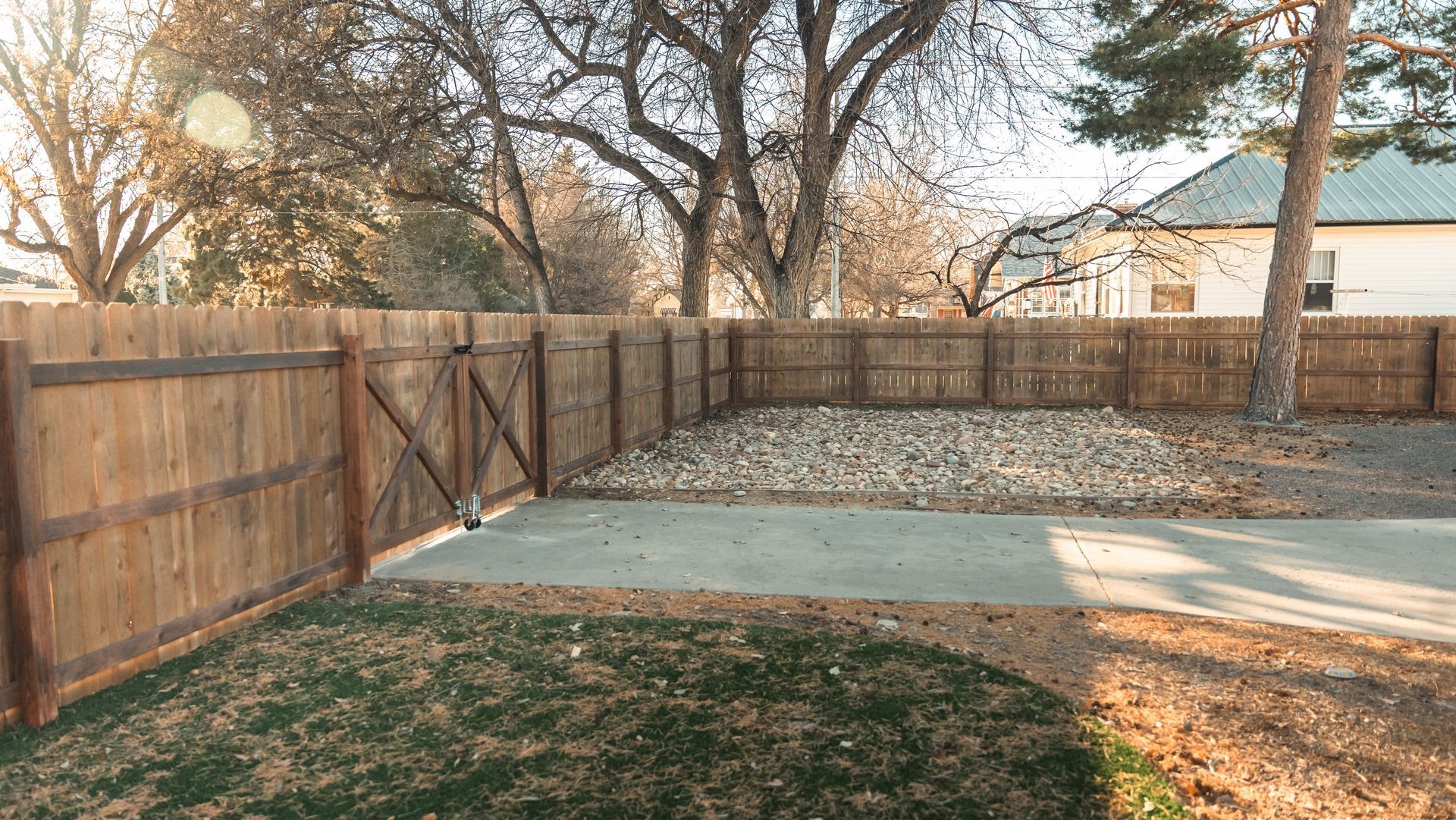 A backyard with a wooden fence and a concrete walkway.