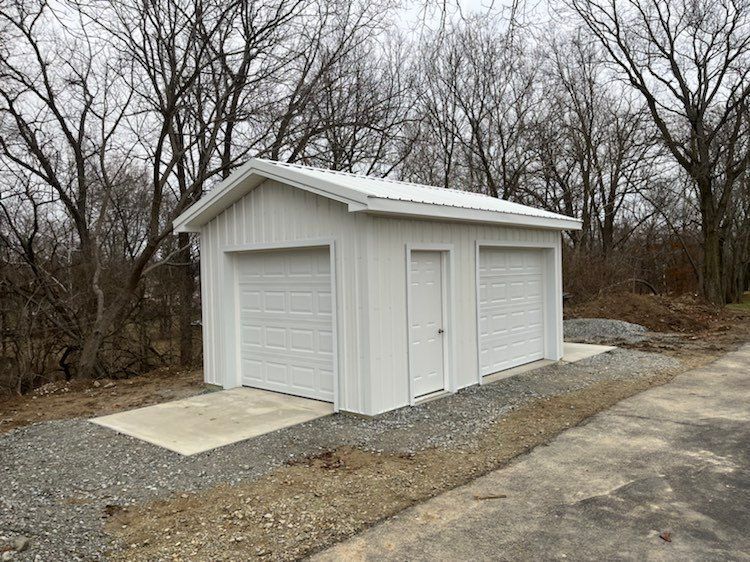 A white garage with two garage doors is sitting next to a gravel road.