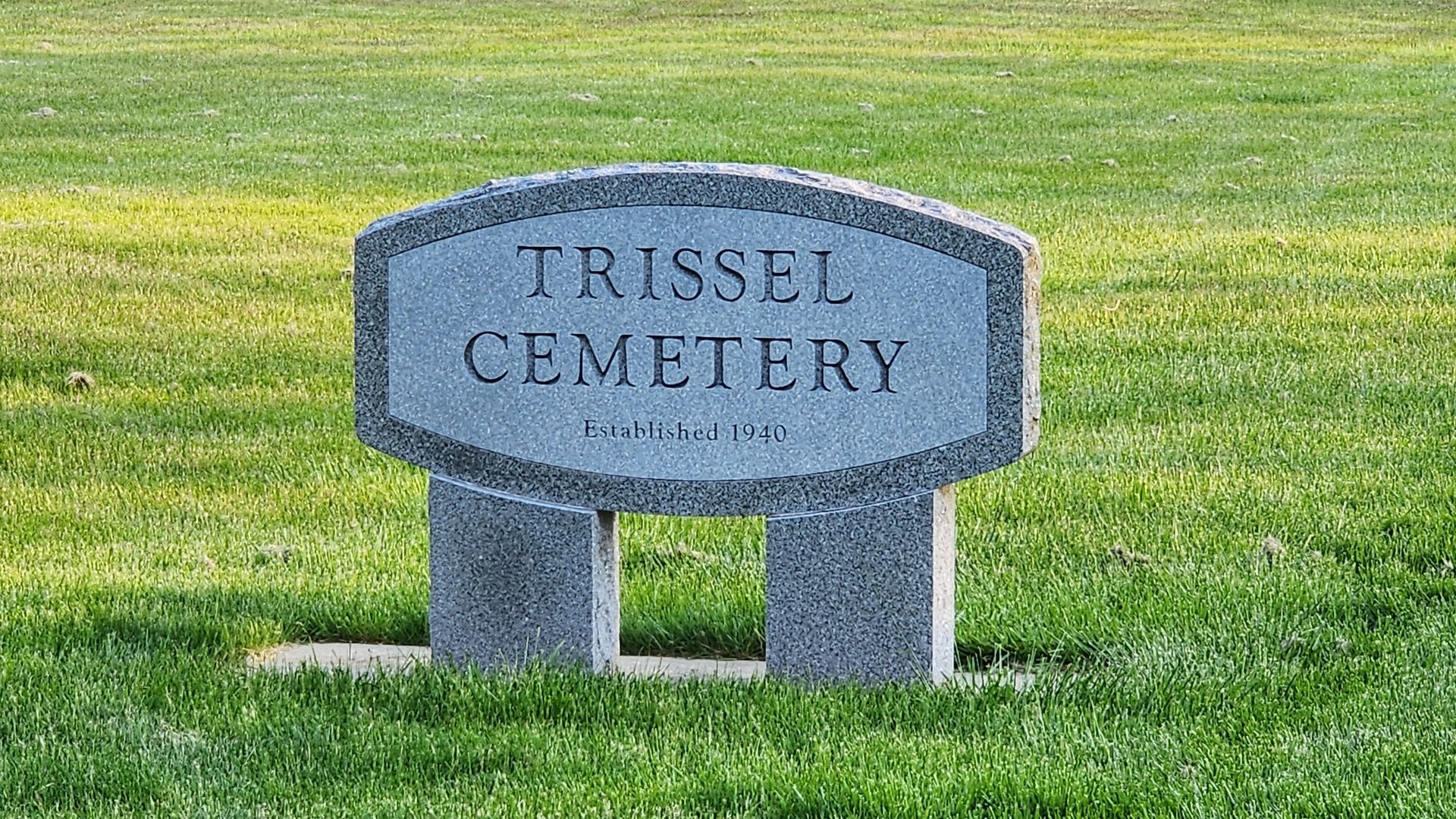 A gravestone for tressel cemetery is in the middle of a lush green field.