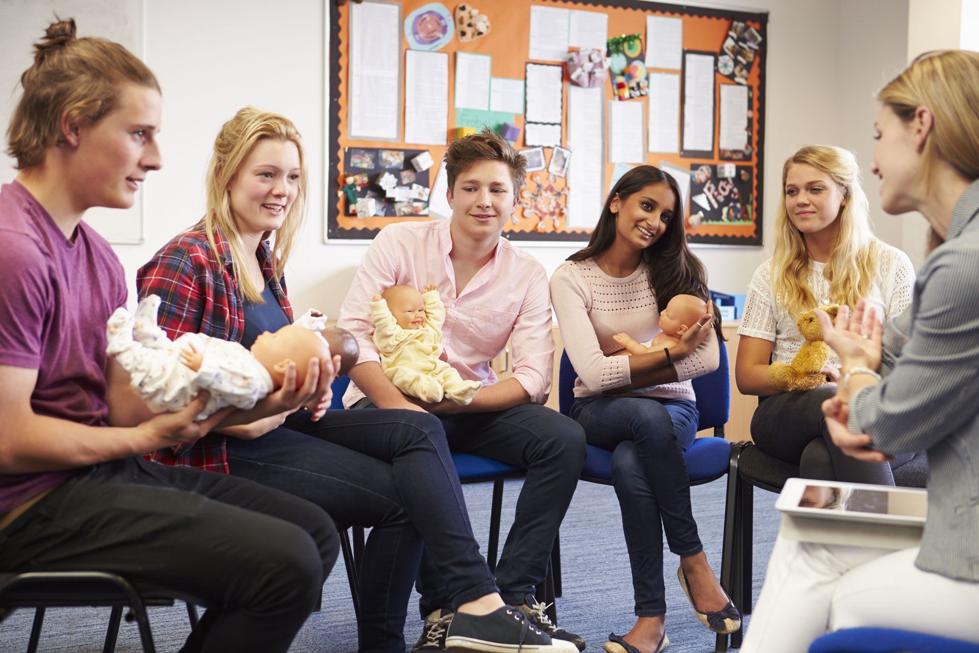 Group of young adults in a circle, learning about babies, with a seated instructor.