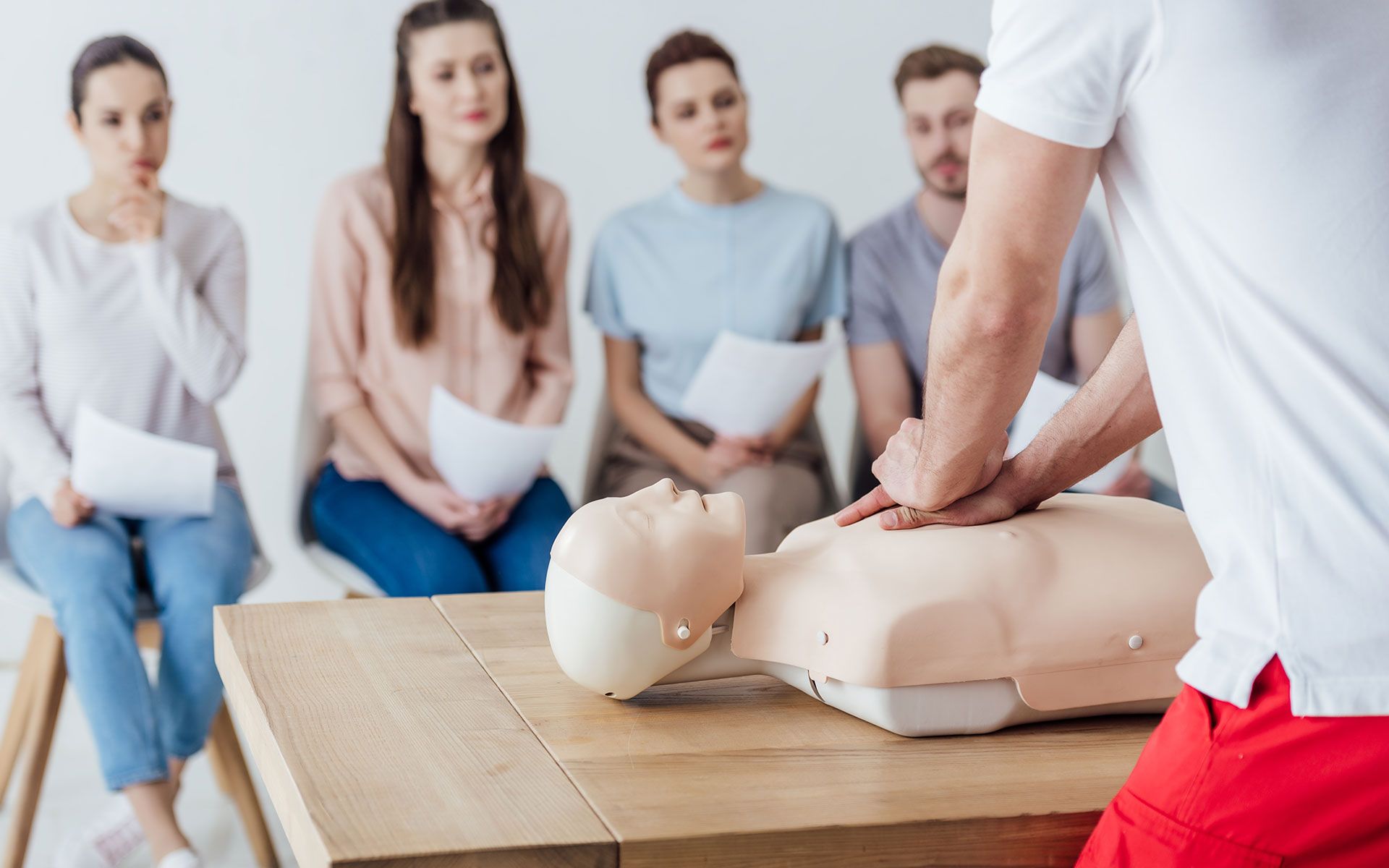 A man is teaching a group of people how to do a cpr on a mannequin.