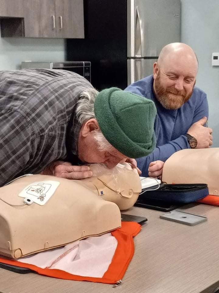 Two men are sitting at a table looking at a mannequin.