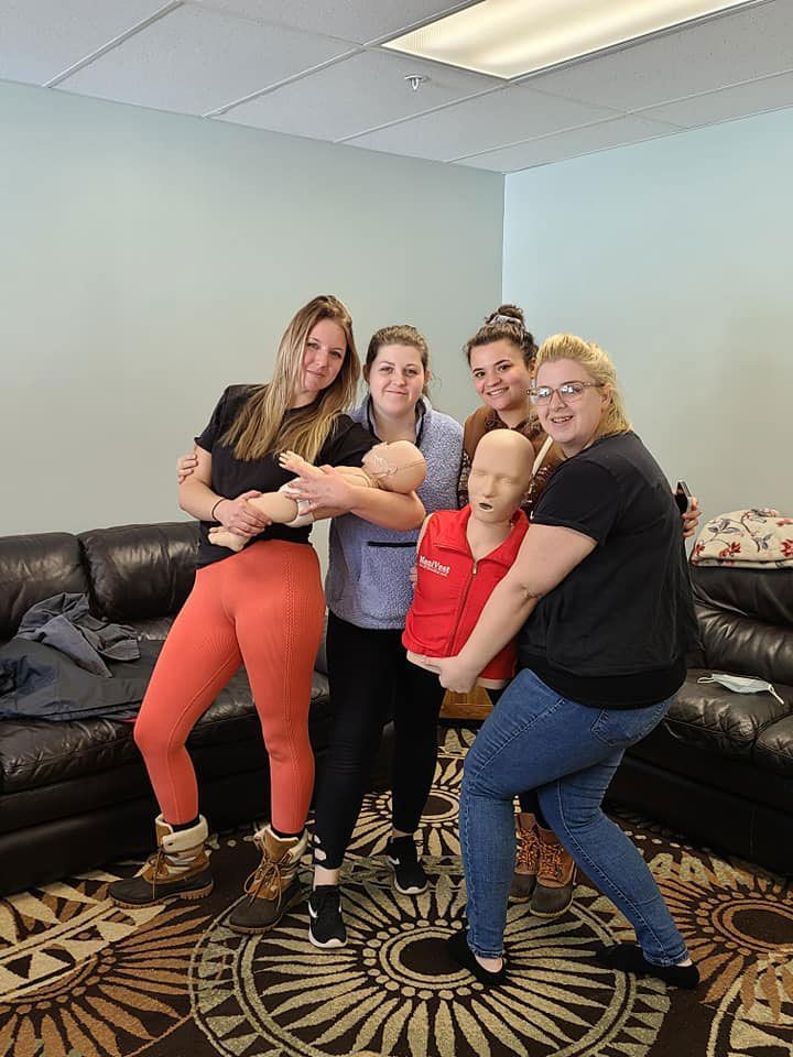 A group of women are standing around a mannequin in a living room.