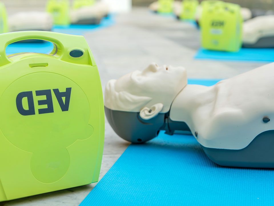 A mannequin is laying on a blue mat next to a green aed device.