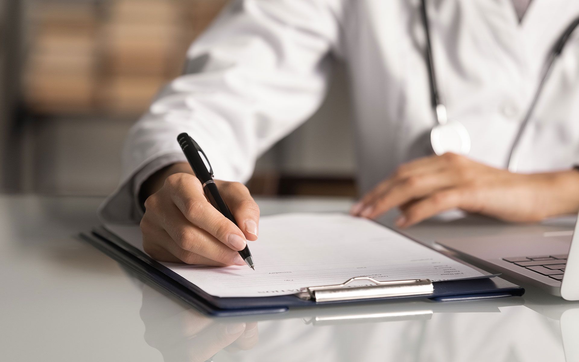 A doctor is writing on a clipboard with a pen.