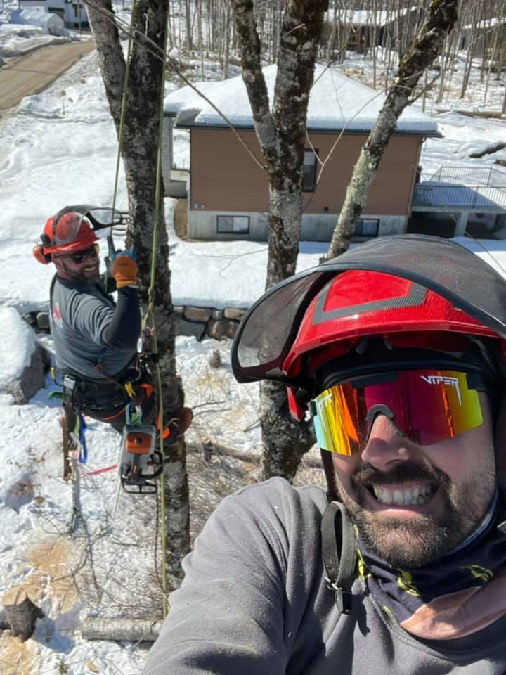 Un homme portant un casque et des lunettes de soleil prend un selfie tout en grimpant à un arbre.