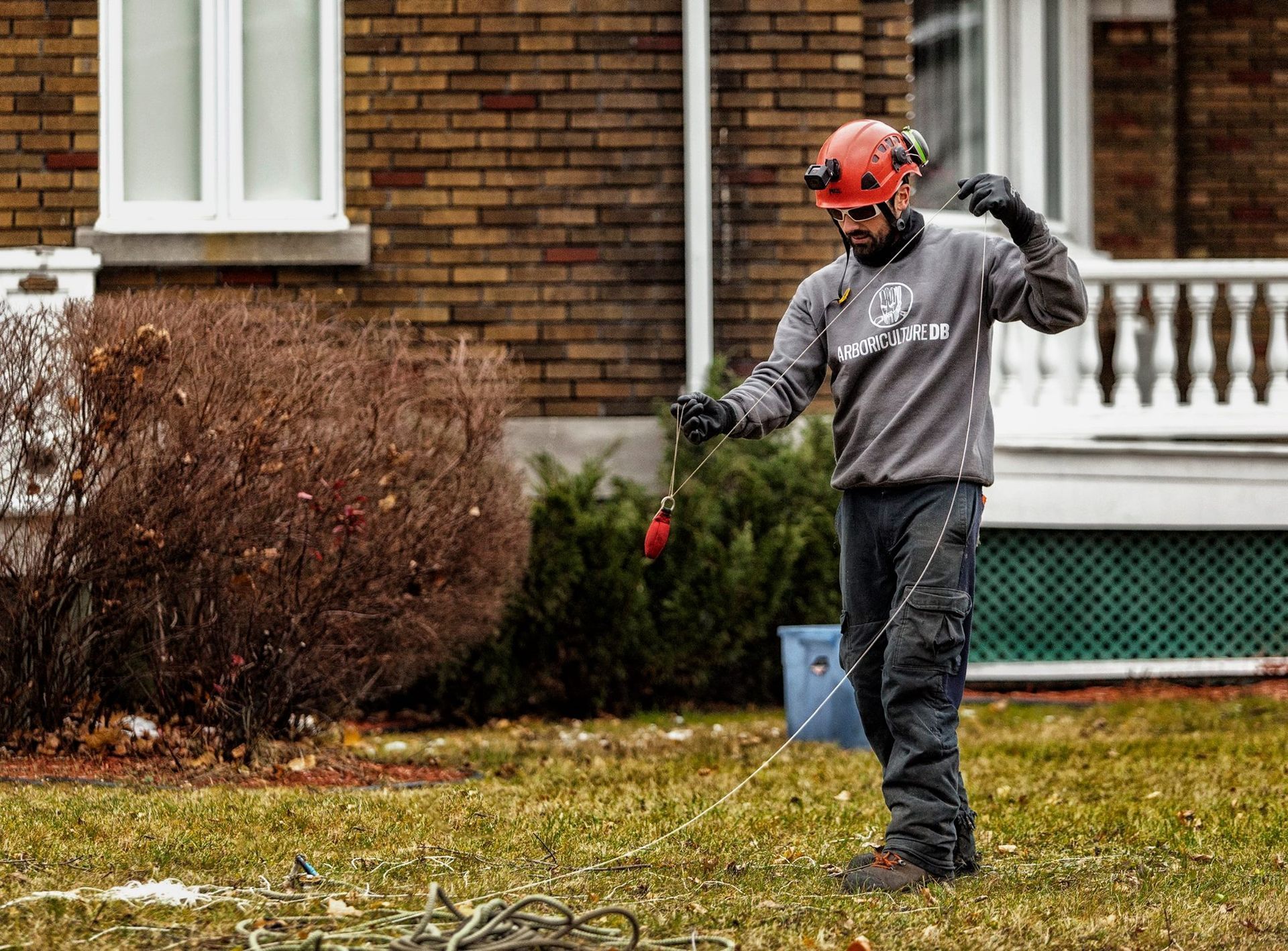Un homme se tient debout dans l'herbe devant un bâtiment en briques tenant une corde.
