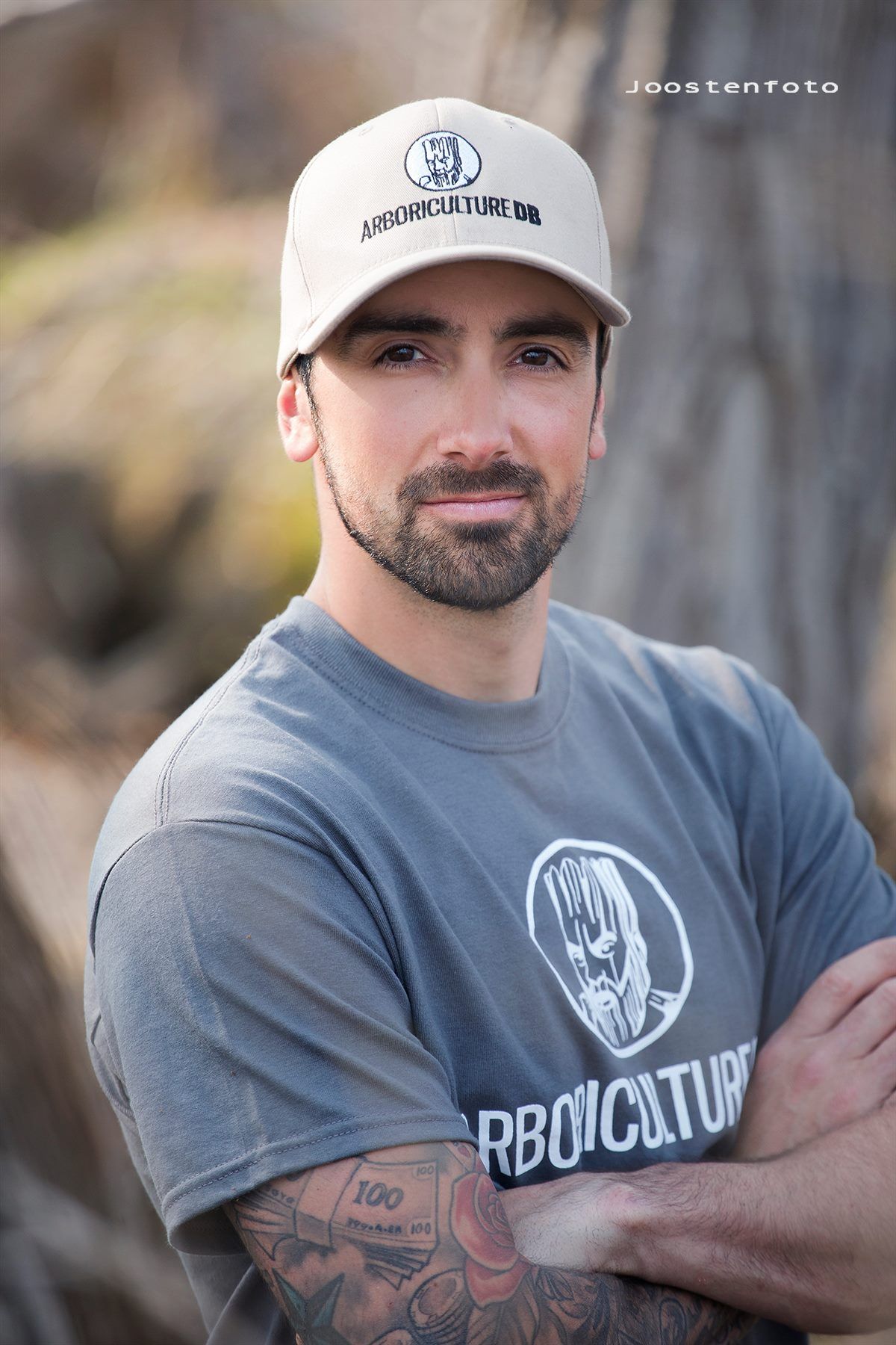 Un homme portant un chapeau et un t-shirt est debout, les bras croisés.