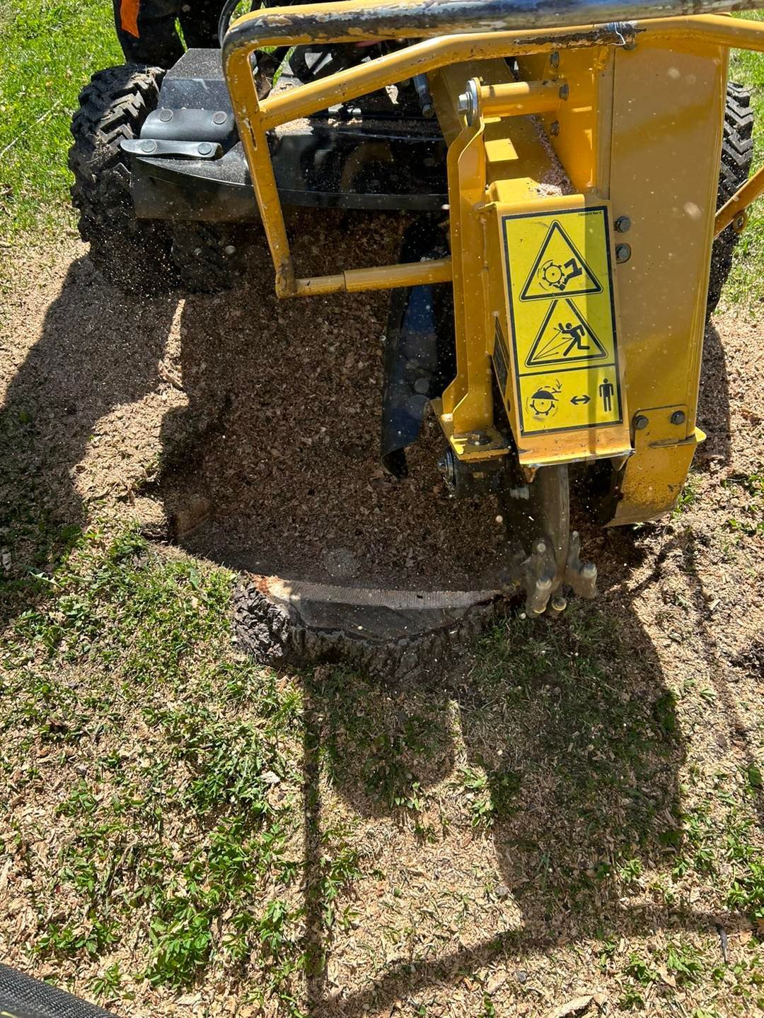Un tracteur jaune coupe une souche d'arbre dans l'herbe.