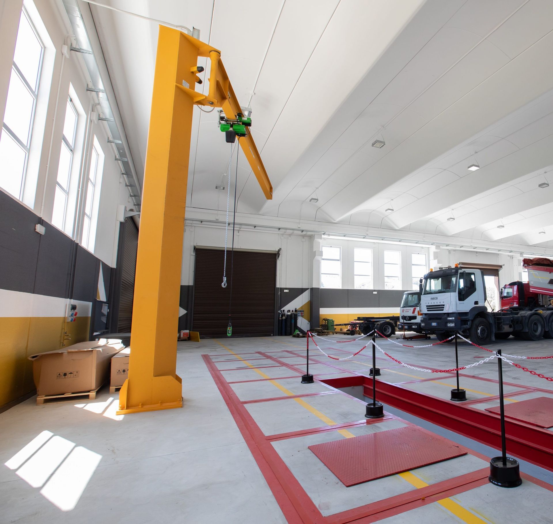 Gru a braccio gialla in una banchina di ispezione per camion; camion sullo sfondo.