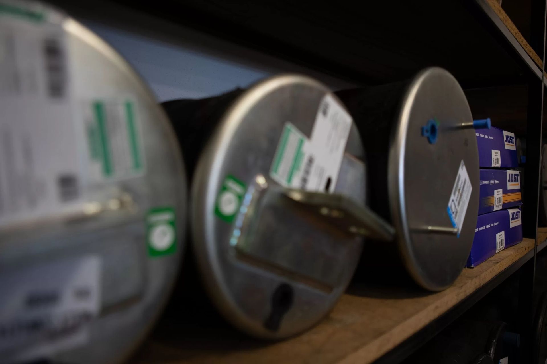 Serbatoi metallici cilindrici con targhette ed etichette su uno scaffale di legno.