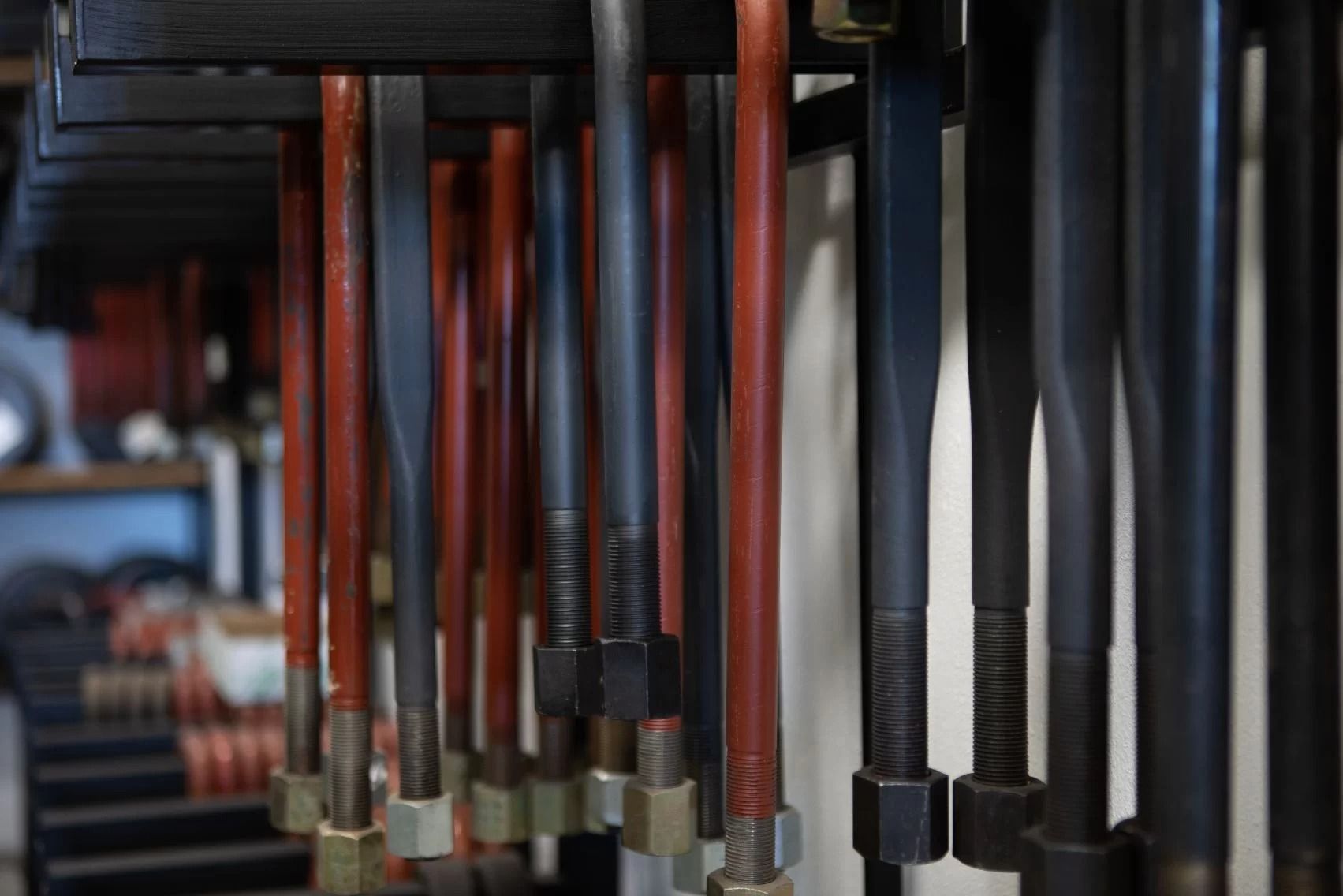 Primo piano di tubi industriali, alcuni neri e altri rossi, appesi a una struttura metallica.