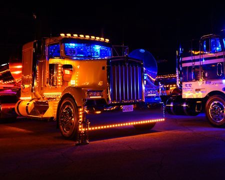 Two semi trucks are parked next to each other at night.