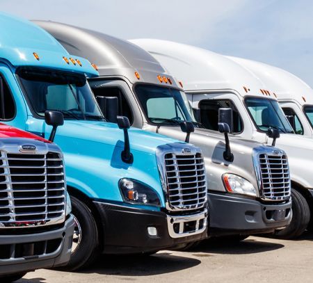 A row of semi trucks are parked in a parking lot.