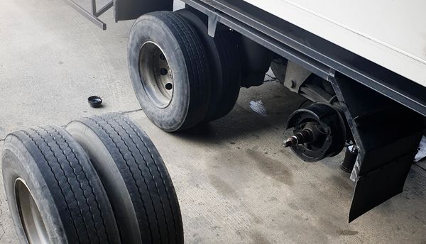 A truck with a broken wheel is sitting in a garage next to a stack of tires.