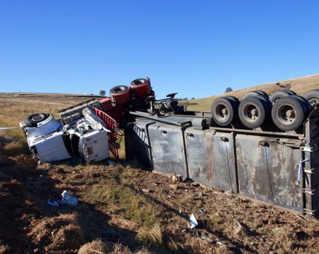 A semi truck has rolled over on its side in a field.