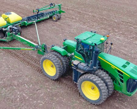 A green tractor is pulling a yellow trailer in a field.