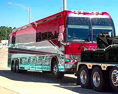 A red and white bus is parked on the side of the road next to a tow truck.