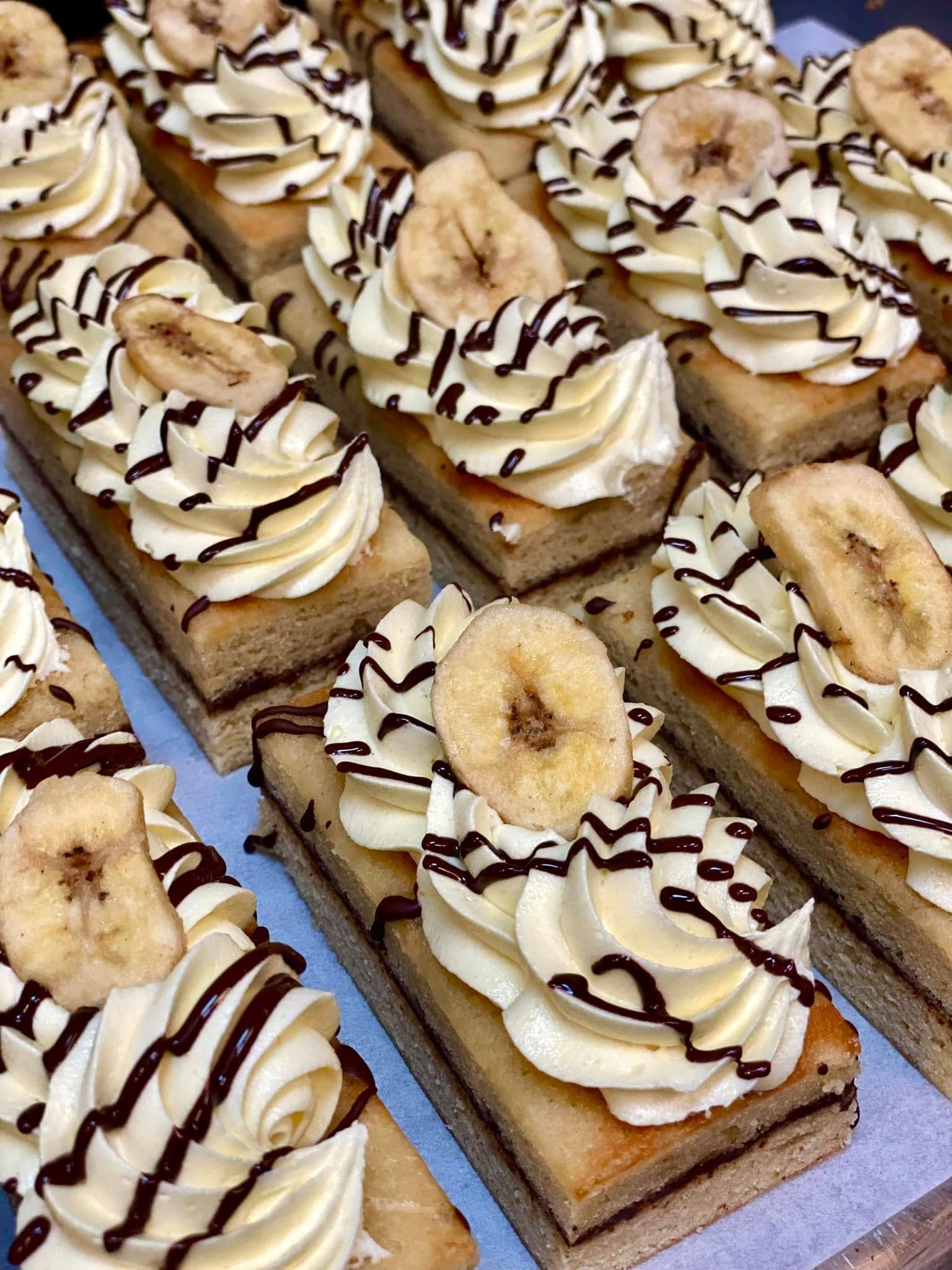 Rows of banana cream cake slices with chocolate drizzle and banana chips.