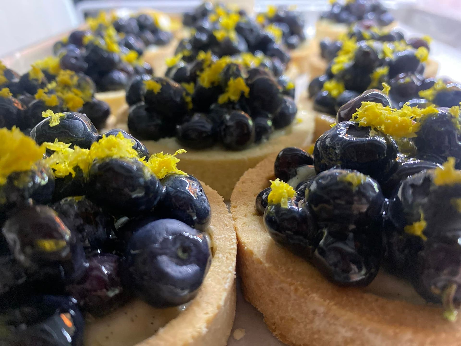 Blueberry tarts topped with lemon zest, arranged on a tray.