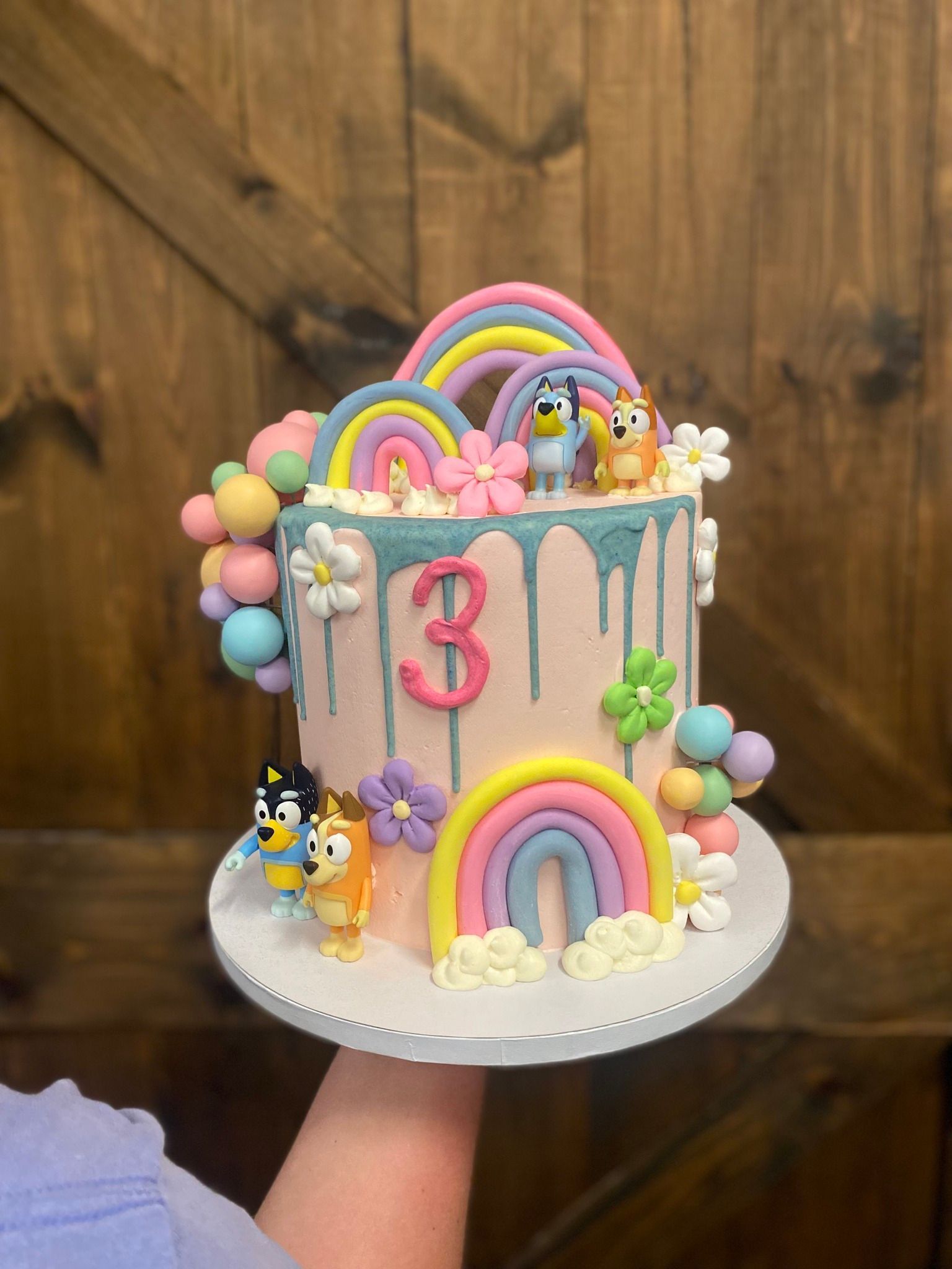 Bluey-themed cake with pastel colors, dripping frosting, rainbow decorations, and figurines.
